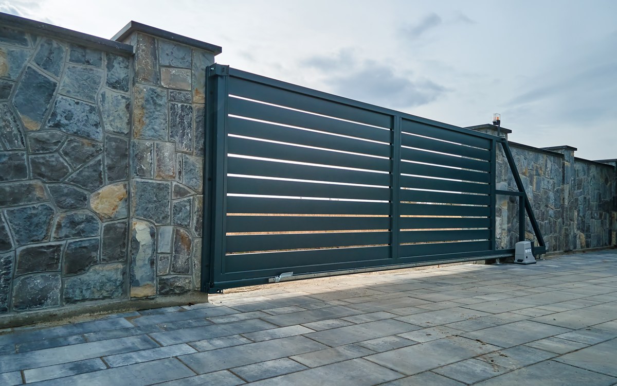 Wide automatic sliding gate with remote control installed in high stone fense wall. Security and protection concept painting metal surfaces - gate