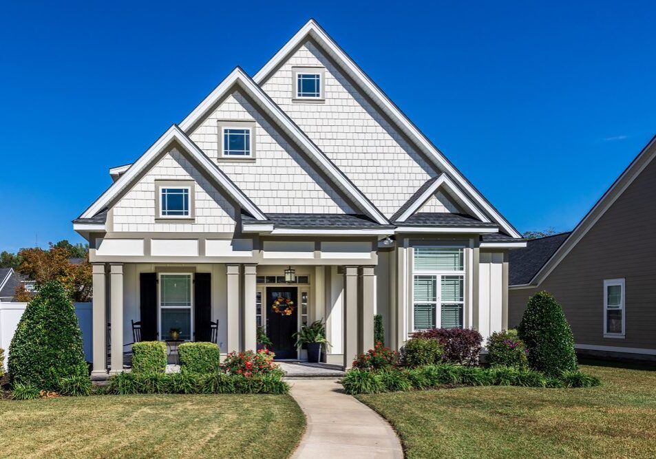 The front view of a new construction cottage craftsman style white house with a triple pitched roof with a sidewalk, landscaping and curb appeal.